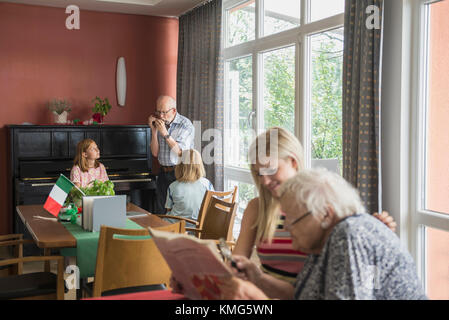 Frau liest Zeitung mit ihrer Mutter, während der Vater bläst Mundharmonika Stockfoto