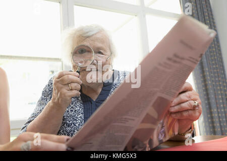 Ältere Frau liest Zeitung mit Lupe Stockfoto