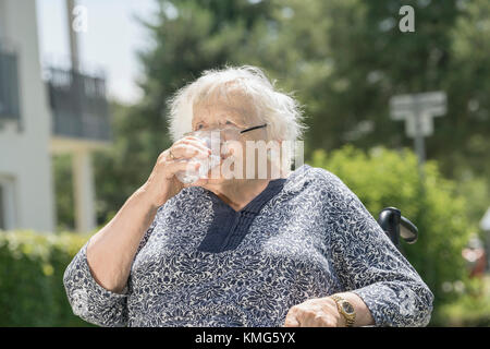 Ältere Frau im Rollstuhl, die ein Glas Wasser trinkt Stockfoto