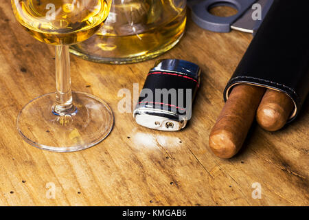 Ledertasche mit Zigarren, Flasche und Glas Whiskey, leichter und Zigarrenabschneider auf einem alten Holz- Board Stockfoto