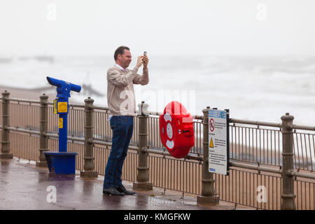 Hastings, East Sussex, UK. 7. Dezember, 2017. Starke Winde verursachen Probleme für einige Leute, dieser Mann macht ein Foto von der tobenden See, kurz bevor es beginnt, unten zu gießen. Foto: Paul Lawrenson/Alamy leben Nachrichten Stockfoto