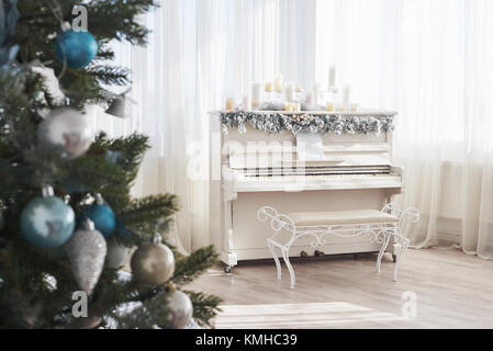 Neujahrsdekoration. Weihnachtsbaum in der Nähe von weißem Klavier am Fensterhintergrund. Stockfoto
