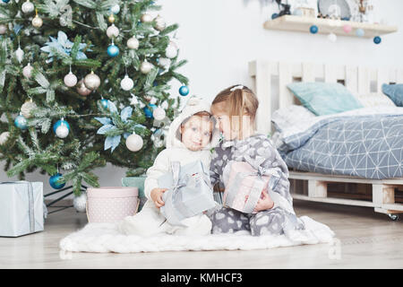 Zwei kleine Schwester Mädchen öffnen ihre Geschenke unter dem Weihnachtsbaum am Morgen auf dem Deck. Stockfoto