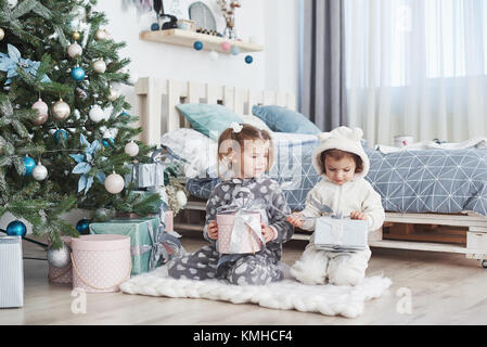 Zwei kleine Schwester Mädchen öffnen ihre Geschenke unter dem Weihnachtsbaum am Morgen auf dem Deck. Stockfoto