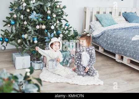 Zwei kleine Schwester Mädchen öffnen ihre Geschenke unter dem Weihnachtsbaum am Morgen auf dem Deck. Stockfoto