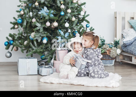 Zwei kleine Schwester Mädchen öffnen ihre Geschenke unter dem Weihnachtsbaum am Morgen auf dem Deck. Stockfoto