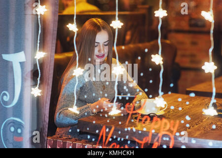 Junge schöne Frau sitzen im Café, Kaffee zu trinken. Magischen Schneefall-Effekt. Weihnachten, Neujahr, Valentinstag, Winter Urlaub Konzept. Das Foto Stockfoto