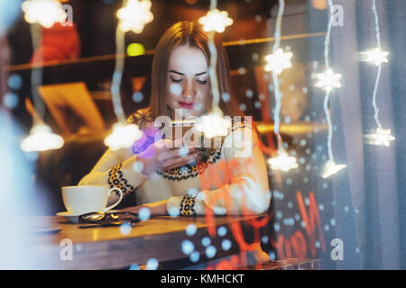 Junge schöne Frau sitzen im Café, Kaffee zu trinken. Magischen Schneefall-Effekt. Weihnachten, Neujahr, Valentinstag, Winter Urlaub Konzept. Das Foto Stockfoto