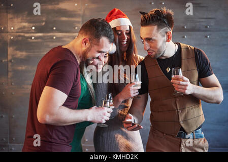 Freundliche alte Freunde untereinander und Telefon Beobachten, Kommunizieren, mit Gläser Champagner im neuen Jahr Partei. Konzept der Unterhaltung und Lifestyle. Stockfoto