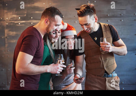 Freundliche alte Freunde untereinander und Telefon Beobachten, Kommunizieren, mit Gläser Champagner im neuen Jahr Partei. Konzept der Unterhaltung und Lifestyle. Stockfoto