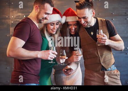 Freundliche alte Freunde untereinander und Telefon Beobachten, Kommunizieren, mit Gläser Champagner im neuen Jahr Partei. Konzept der Unterhaltung und Lifestyle. Stockfoto