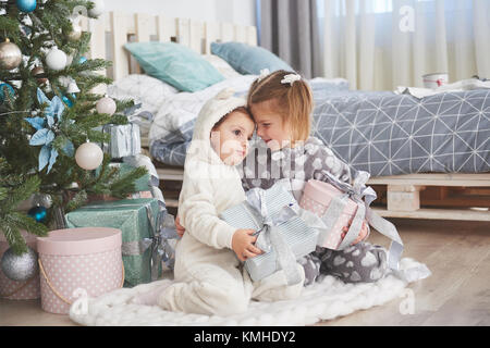 Zwei kleine Schwester Mädchen öffnen ihre Geschenke unter dem Weihnachtsbaum am Morgen auf dem Deck Stockfoto