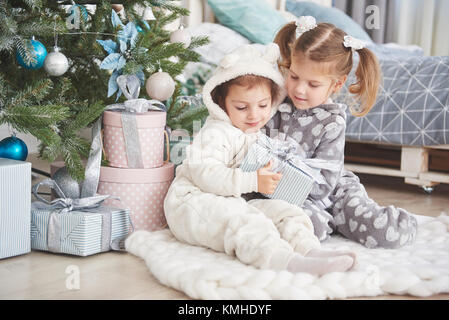 Zwei kleine Schwester Mädchen öffnen ihre Geschenke unter dem Weihnachtsbaum am Morgen auf dem Deck Stockfoto