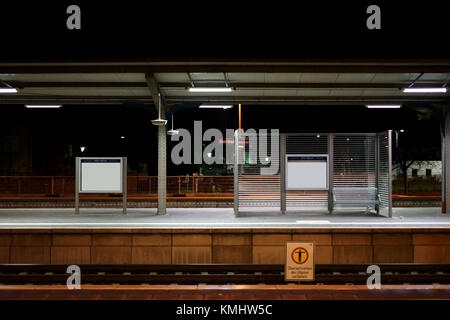 Die Plattform der Weinheimer Bahnhof bei Nacht mit Sitzgelegenheiten auf einer Glastrennwand. Stockfoto