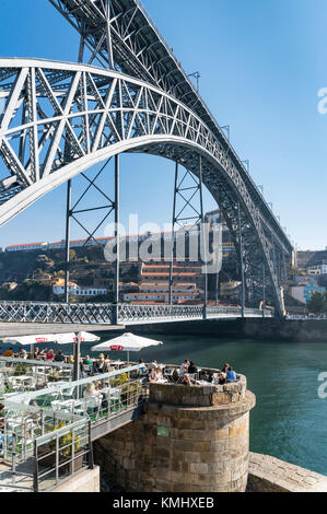 Cafe Bar auf der Cais da Ribeira, neben dem Fluss Ufer des Douro in der Ribeira Viertel von Porto, Portugal. Mit dem Dom Luis I Brücke in backgrou Stockfoto