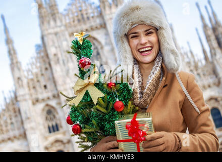 Spaß Weihnachten Reise nach Mailand, Italien. Lächeln moderne Frau in Mailand, Italien mit Weihnachtsbaum und Geschenk Stockfoto