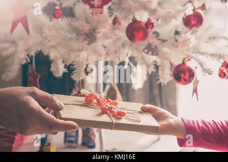 Großeltern gibt Weihnachtsgeschenk für kleine Mädchen, weihnachtsbaumschmuck im Hintergrund, getönt Stockfoto