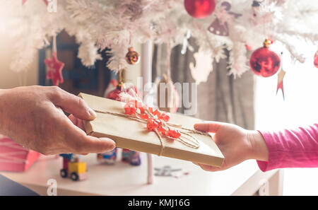 Großeltern gibt Weihnachtsgeschenk für kleine Mädchen, weihnachtsbaumschmuck im Hintergrund Stockfoto