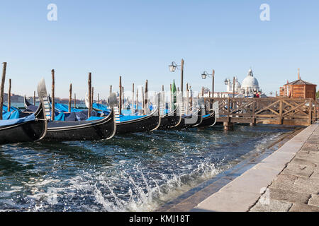 Gondeln an San Marco Reiten hoch im Wasser auf einem Acqua Alta Tide mit Splash und Blick auf Baslica di Santa Maria della Salaute, Venedig, Italien Stockfoto