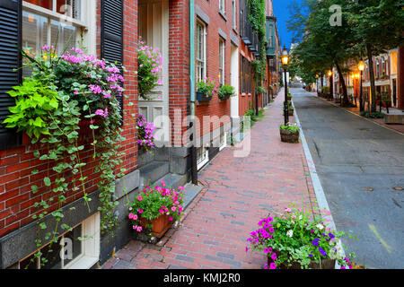 Charmante Straße in Beacon Hill, Boston. Gebäude aus rotem Ziegel und Bürgersteige, Straßenlaternen, Blumenkästen und Pflanzer, Nacht. Stockfoto