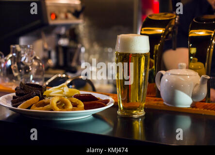 Die Tasse helles Bier und einen Teller mit Snacks an der Bar Stockfoto