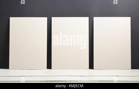 Eine Vorlage für ein Modell von drei Poster auf einem schwarzen Hintergrund und eine hölzerne Tabelle. Weiß leer für Sample Design. Stockfoto