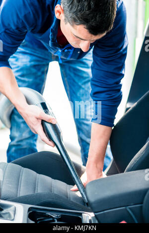 Junge hart arbeitender Mann mit Vakuum für die Reinigung der Innenraum eines Autos bei Auto waschen Stockfoto