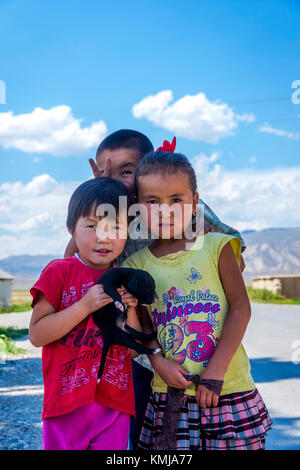 UGUT, KIRGISISTAN - AUGUST 16: Einheimische kirgisische Kinder posieren mit einem Welpen in einem abgelegenen Dorf. Ugut ist ein abgelegenes Dorf in Kirgisistan. August 2016 Stockfoto