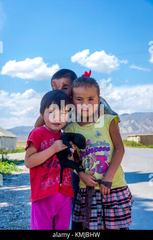 UGUT, KIRGISISTAN - AUGUST 16: Einheimische kirgisische Kinder posieren mit einem Welpen in einem abgelegenen Dorf. Ugut ist ein abgelegenes Dorf in Kirgisistan. August 2016 Stockfoto