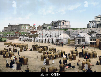 Dieses historische Bild zeigt den Strand von Scheveningen in den Niederlanden um 1900 und zeigt die Strandszene aus dem frühen 20. Jahrhundert mit historischen Kleidern und typischen Aktivitäten am Meer. Stockfoto
