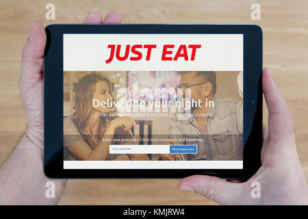 Ein Mann schaut auf die nur Essen Website auf seinem iPad tablet device, Schuß gegen einen hölzernen Tisch top Hintergrund (nur redaktionelle Nutzung) Stockfoto