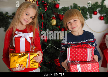 Porträt von zwei glückliche Kinder mit Weihnachten Geschenkboxen und Dekorationen. Zwei Kinder zu Hause in Stockfoto