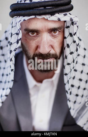 Portrait einer wütend und intensiven muslimisch-arabischen Mann mit einem roten Bart trägt einen schwarzen und weißen muslimischen Kopfbedeckung und einen grauen Anzug mit weißem Kleid Shirt Stockfoto