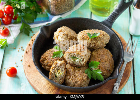 Hausgemachte Frikadellen mit Buchweizen und ei Füllung. Gusseiserne Pfanne mit lecker gebratene Koteletts, frische Kräuter und Gemüse auf dem Küchentisch Stockfoto