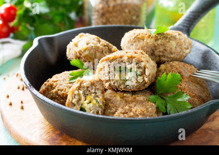 Hausgemachte Frikadellen mit Buchweizen und ei Füllung. Gusseiserne Pfanne mit lecker gebratene Koteletts, frische Kräuter und Gemüse auf dem Küchentisch Stockfoto