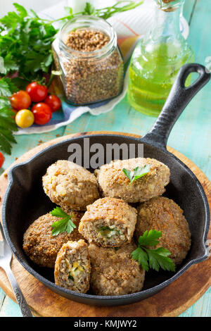 Hausgemachte Frikadellen mit Buchweizen und ei Füllung. Gusseiserne Pfanne mit lecker gebratene Koteletts, frische Kräuter und Gemüse auf dem Küchentisch Stockfoto