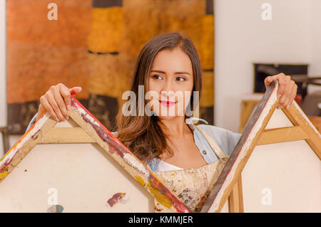 Schöne Frau Maler halten in ihren Händen einen leeren Rahmen in einem Studio Farbe Hintergrund, Kunst Kurse für Erwachsene, Bildung Konzept Stockfoto