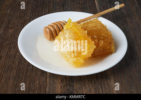 Goldene Honigwabe, Honig Stick auf einem weißen Teller auf vintage Holztisch Stockfoto