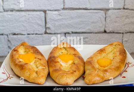 Khachapuri Adschariens auf Platte und mit rustikalen Hintergrund. Torte mit Mozzarella und Ei öffnen. Stockfoto