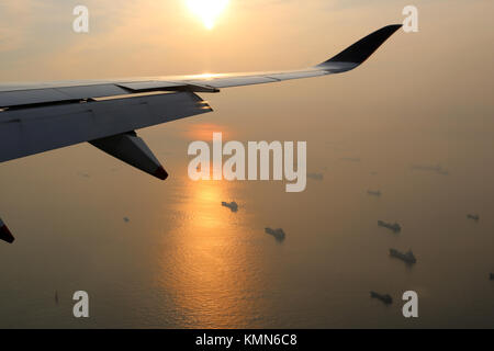 Blick aus dem Flugzeug von flugzeugflügel über Sonnenaufgang über Singapur Meerenge mit Schiffen, die in das Wasser unten verankert. Sunrise spiegelt auch das Wasser. Stockfoto