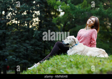 Foto von unten der sitzende Frau mit Hund auf dem grünen Rasen Stockfoto