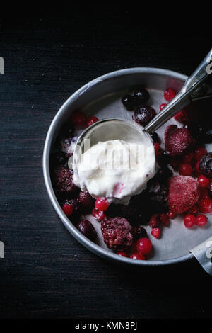 Aluminium-Platte mit Vanille-Eis und gefrorenen Beeren-Mix mit Metalllöffel über schwarzen Tisch serviert Stockfoto