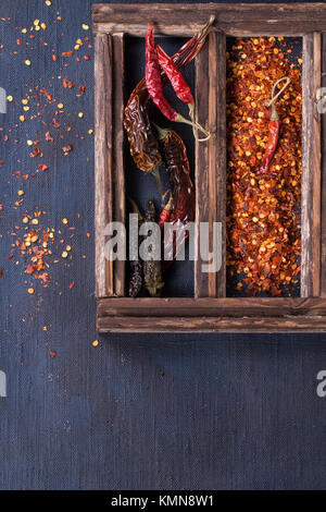 Sortiment von getrocknet ganze und Flocken red hot Chili Peppers in Holzkiste über dunkel blauem Segeltuch als Hintergrund Stockfoto
