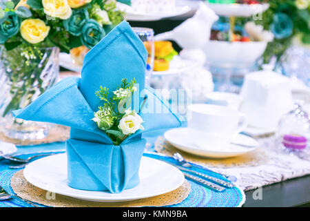 Party Tisch mit einem blau serviette, Blume, weiße Platte und weiß Teetasse in der Feier Tag. Dekoration Tisch in Blau Ton Farbe serviert. Stockfoto