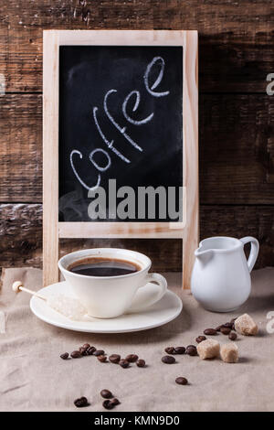 Tasse Kaffee mit Tafel auf Tisch mit Zucker und Kaffee Bohnen. Serien ansehen Stockfoto