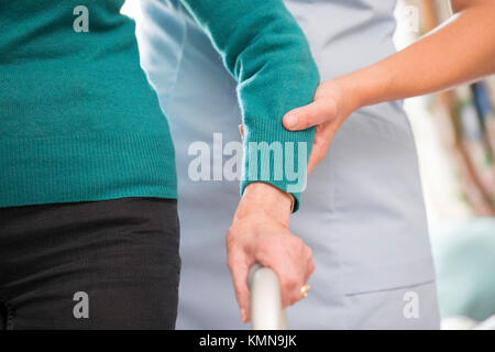 Die ältere Frau Hände auf Gehhilfe mit Sorgfalt Arbeiter im Hintergrund Stockfoto