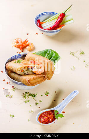 Frittierte Frühlingsrollen mit Gemüse und Garnelen, serviert mit pikanter Sauce über weißen hölzernen Hintergrund. Stockfoto