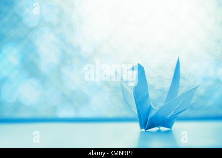 Origami Papier Vogel auf das hell beleuchtete Fenster aus Glas mit blauen solf Licht und Bokeh, selektive konzentrieren. Stockfoto