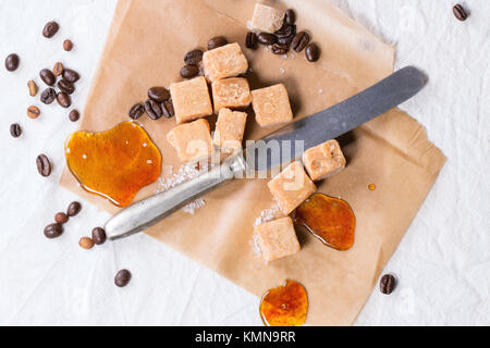 Fudge Candy, Kaffeebohnen und Karamell auf Backpapier, diente über weiße Tischdecke mit Vintage Messer Stockfoto