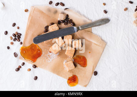 Fudge Candy, Kaffeebohnen und Karamell auf Backpapier, diente über weiße Tischdecke mit Vintage Messer Stockfoto